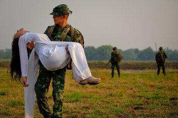 Soft blur of soldier man carry Vietnamese woman in the field also have soldier team as background...