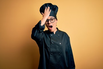 Young beautiful brunette chef woman wearing cooker uniform and hat over yellow background surprised with hand on head for mistake, remember error. Forgot, bad memory concept.