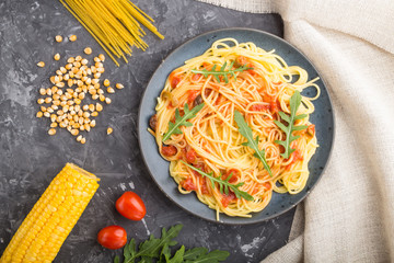 Corn noodles with tomato sauce and arugula on a black concrete background. Top view, close up.