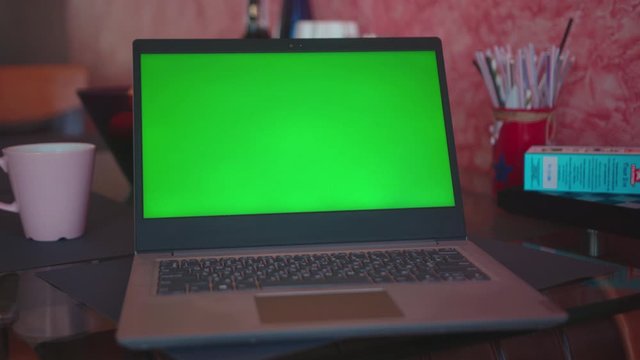 On the table laptop computer with green screen on table at home blank communication notebook display internet table technology monitor keyboard coffee online slow motion