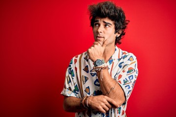 Young handsome man on vacation wearing summer shirt over isolated red background Thinking worried about a question, concerned and nervous with hand on chin