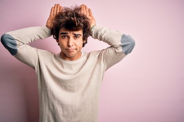 Young handsome man wearing casual t-shirt standing over isolated pink background Doing bunny ears gesture with hands palms looking cynical and skeptical. Easter rabbit concept.