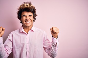 Young handsome man wearing king crown standing over isolated pink background very happy and excited...