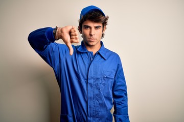 Young mechanic man wearing blue cap and uniform standing over isolated white background looking...
