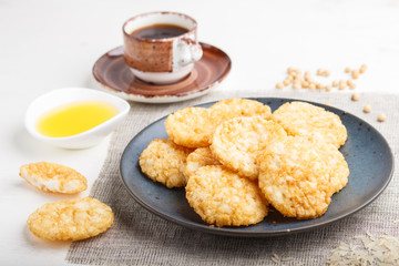 Traditional japanese rice chips cookies with honey and soy sauce on a blue ceramic plate and a cup of coffee on a white wooden background. side view, selective focus.