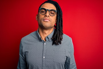 Fototapeta premium Young handsome african american man with dreadlocks wearing casual shirt and glasses Relaxed with serious expression on face. Simple and natural looking at the camera.