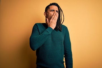 Fototapeta premium Young handsome african american afro man with dreadlocks wearing green casual sweater bored yawning tired covering mouth with hand. Restless and sleepiness.