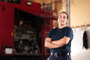 Professional fireman portrait. Female firefighter wearing uniform of shirt and trousers. Fire truck in the background.