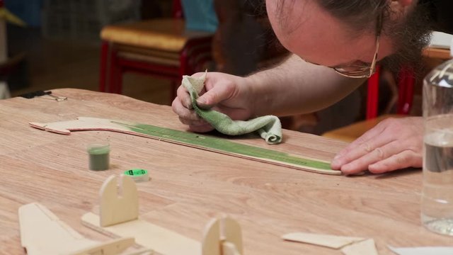 bearded master in glasses colours vintage airplane fuselage model in green and checks on table at masterclass slow motion