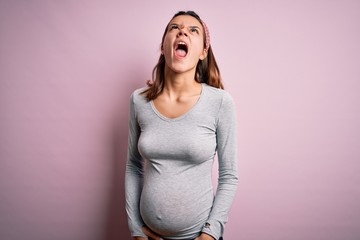 Young beautiful teenager girl pregnant expecting baby over isolated pink background angry and mad...