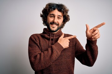 Young handsome man with beard wearing casual sweater standing over white background smiling and looking at the camera pointing with two hands and fingers to the side.