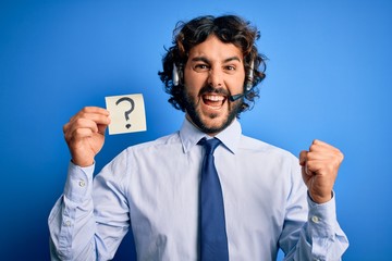 Young call center agent man with beard working using headset holding question mark reminder screaming proud and celebrating victory and success very excited, cheering emotion
