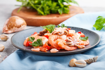 Boiled shrimps or prawns and small octopuses with herbs on a blue ceramic plate on a gray concrete background. Side view, selective focus.