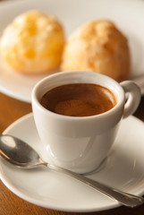 cup of espresso coffee viewed from the front with cheese breads in the background