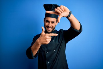Young handsome chef man with beard wearing cooker uniform and hat over blue background smiling...
