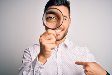 Fototapeta na wymiar Young detective man looking through magnifying glass over isolated background with surprise face pointing finger to himself