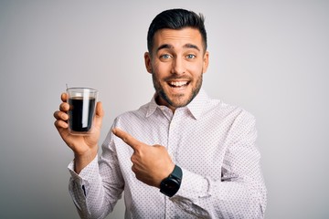 Young handsome man drinking a cup of hot coffee over white isolated background very happy pointing with hand and finger