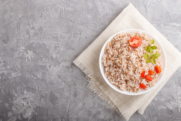 Unpolished rice porridge in white bowl on a gray concrete background. Top view, copy space.