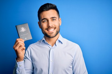 Young handsome tourist man holding australia australian passport id over blue background with a...