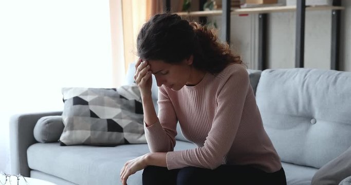Worried upset young woman sitting on sofa anxious about problem, suffers from mental stress, regrets mistake. Depressed girl thinking of loneliness, feels guilt, makes difficult decision concept.