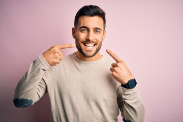 Young handsome man wearing casual sweater standing over isolated pink background smiling cheerful showing and pointing with fingers teeth and mouth. Dental health concept.