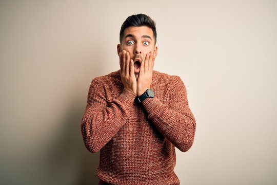 Young handsome man wearing casual sweater standing over isolated white background afraid and shocked, surprise and amazed expression with hands on face