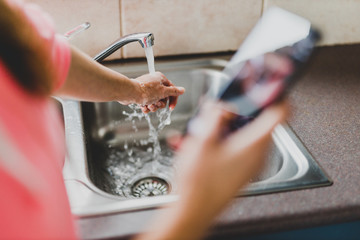 flattening the curve through hygiene against covid-19, woman washing her hands while scrolling social media or news on her smartphone