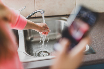 flattening the curve through hygiene against covid-19, woman washing her hands while scrolling social media or news on her smartphone