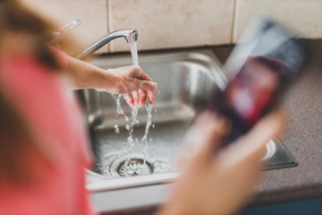 flattening the curve through hygiene against covid-19, woman washing her hands while scrolling social media or news on her smartphone