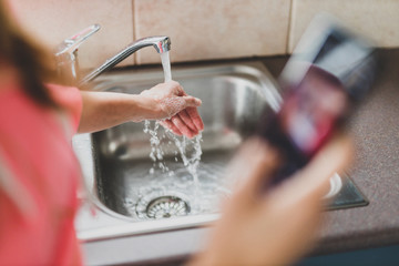 flattening the curve through hygiene against covid-19, woman washing her hands while scrolling social media or news on her smartphone