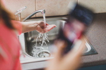 flattening the curve through hygiene against covid-19, woman washing her hands while scrolling social media or news on her smartphone