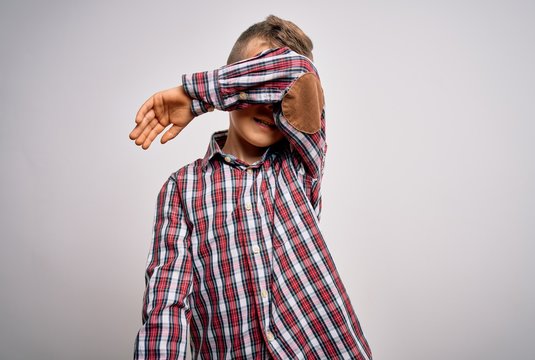Young little caucasian kid with blue eyes wearing elegant shirt standing over isolated background covering eyes with arm smiling cheerful and funny. Blind concept.