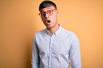 Young handsome hispanic business man wearing nerd glasses over yellow background afraid and shocked with surprise expression, fear and excited face.