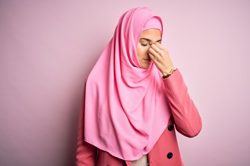 Young beautiful girl wearing muslim hijab standing over isolated pink background tired rubbing nose and eyes feeling fatigue and headache. Stress and frustration concept.