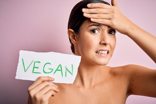 Young beautiful girl holding paper with vegan message over isolated pink background stressed with hand on head, shocked with shame and surprise face, angry and frustrated. Fear and upset for mistake.
