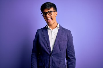 Fototapeta premium Young handsome business man wearing jacket and glasses over isolated purple background winking looking at the camera with sexy expression, cheerful and happy face.