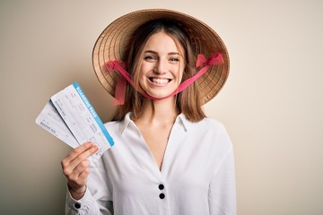 Young beautiful redhead tourist woman wearing asian traditional hat holding boarding pass with a happy face standing and smiling with a confident smile showing teeth