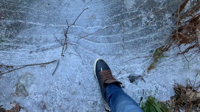 The person walks in sneakers on the frozen pools and breaks ice, jeans trousers, blue color