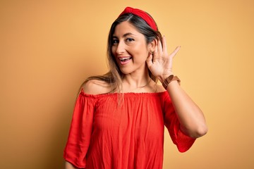 Young beautiful woman colorful summer style over yellow isolated background smiling with hand over ear listening an hearing to rumor or gossip. Deafness concept.