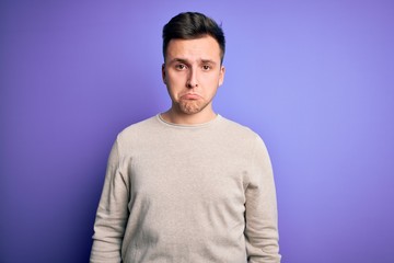 Young handsome caucasian man wearing casual sweater over purple isolated background depressed and worry for distress, crying angry and afraid. Sad expression.