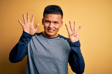 Young handsome latin man wearing casual t-shirt standing over yellow background showing and pointing up with fingers number nine while smiling confident and happy.