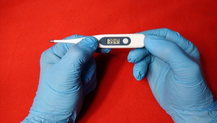 Gloves hands holding a thermometer indicating fever