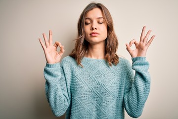 Young blonde girl wearing casual blue winter sweater over isolated background relax and smiling with eyes closed doing meditation gesture with fingers. Yoga concept.