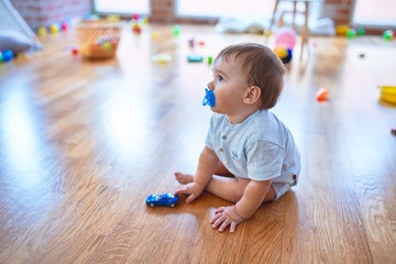 Adorable toddler sitting on the floor using pacifier playing around lots of toys at kindergarten