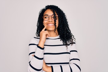Young african american woman wearing striped sweater and glasses over white background with hand on chin thinking about question, pensive expression. Smiling with thoughtful face. Doubt concept.