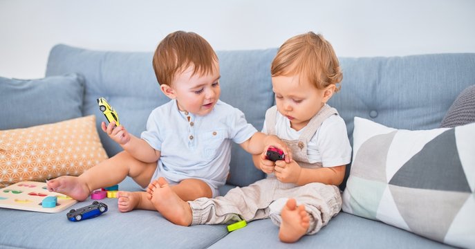 Beautiful toddlers sitting on the sofa playing with toys at home
