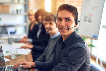 Group of call center workers working together with smile on face using headset. Young handsome man smiling at the office.