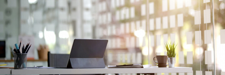 Cropped shot of portable workspace with digital tablet, supplies and stationery in glass wall co-working space