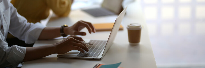 Cropped shot of businessman typing on laptop with coffee cup in co-working space
