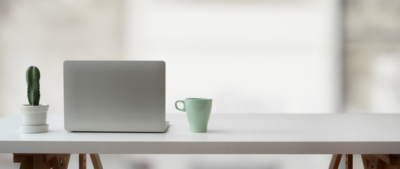 Cropped shot of simple workspace with laptop, cactus pot, mug and copy space on white table